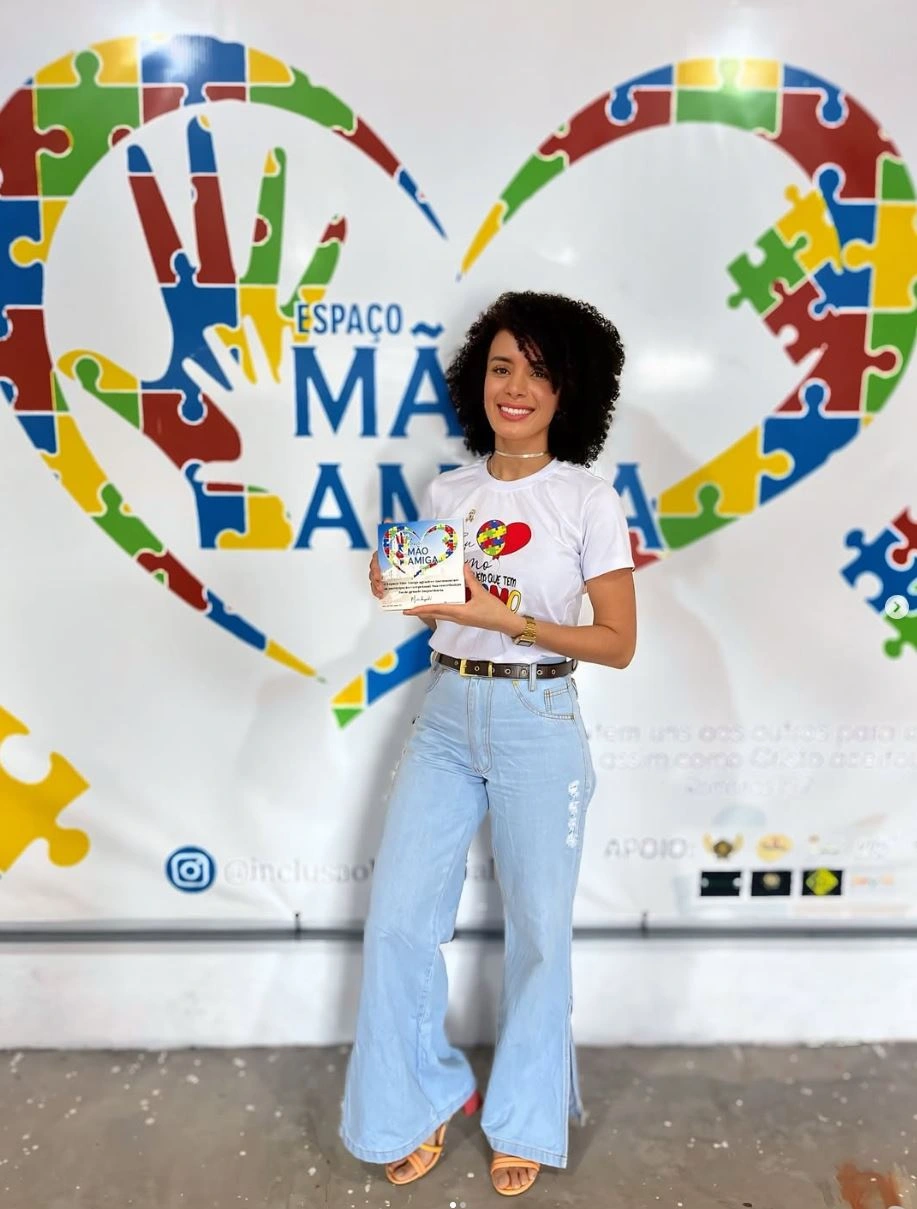 Dra. Bruna Pires segurando uma homenagem diante do painel do Espaço Mão Amiga